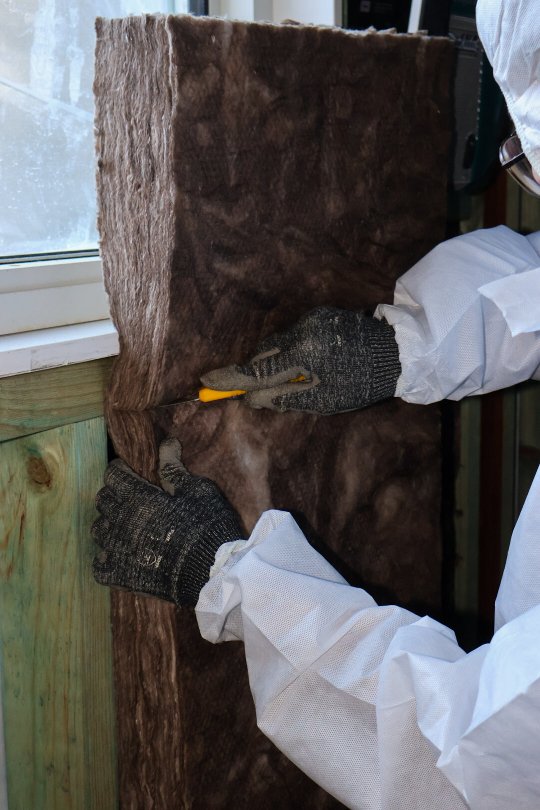 Installer trimming wall insulation batt into timber wall framing
